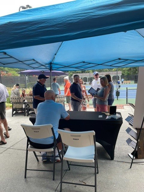 Guests gathering under blue tents beside the courts as Mark signs books