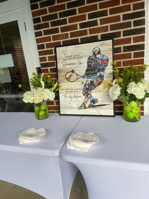 A framed tennis print and flowers with tennis balls decorating the signing table